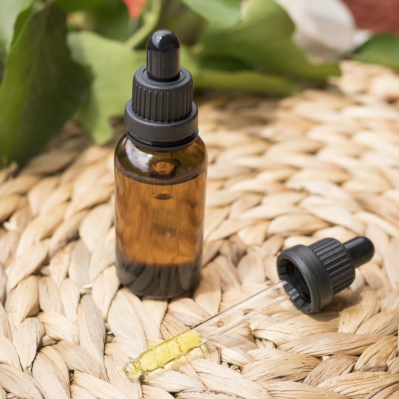 Brown glass tincture bottle with black cap on a woven surface with blurred greenery in the background